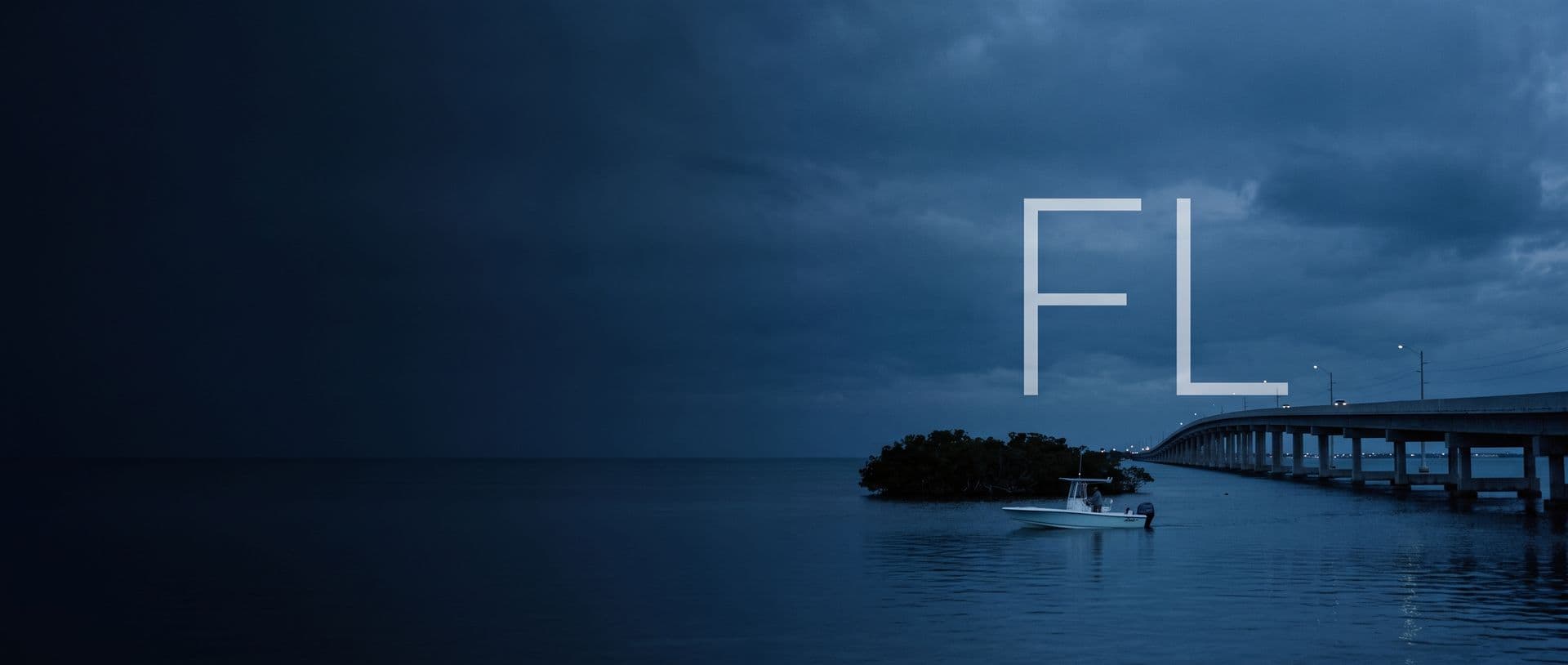 The Seven Mile Bridge in the Florida Keys at dusk, a centre-console boat on the flats beneath it, with the letters FL in the sky