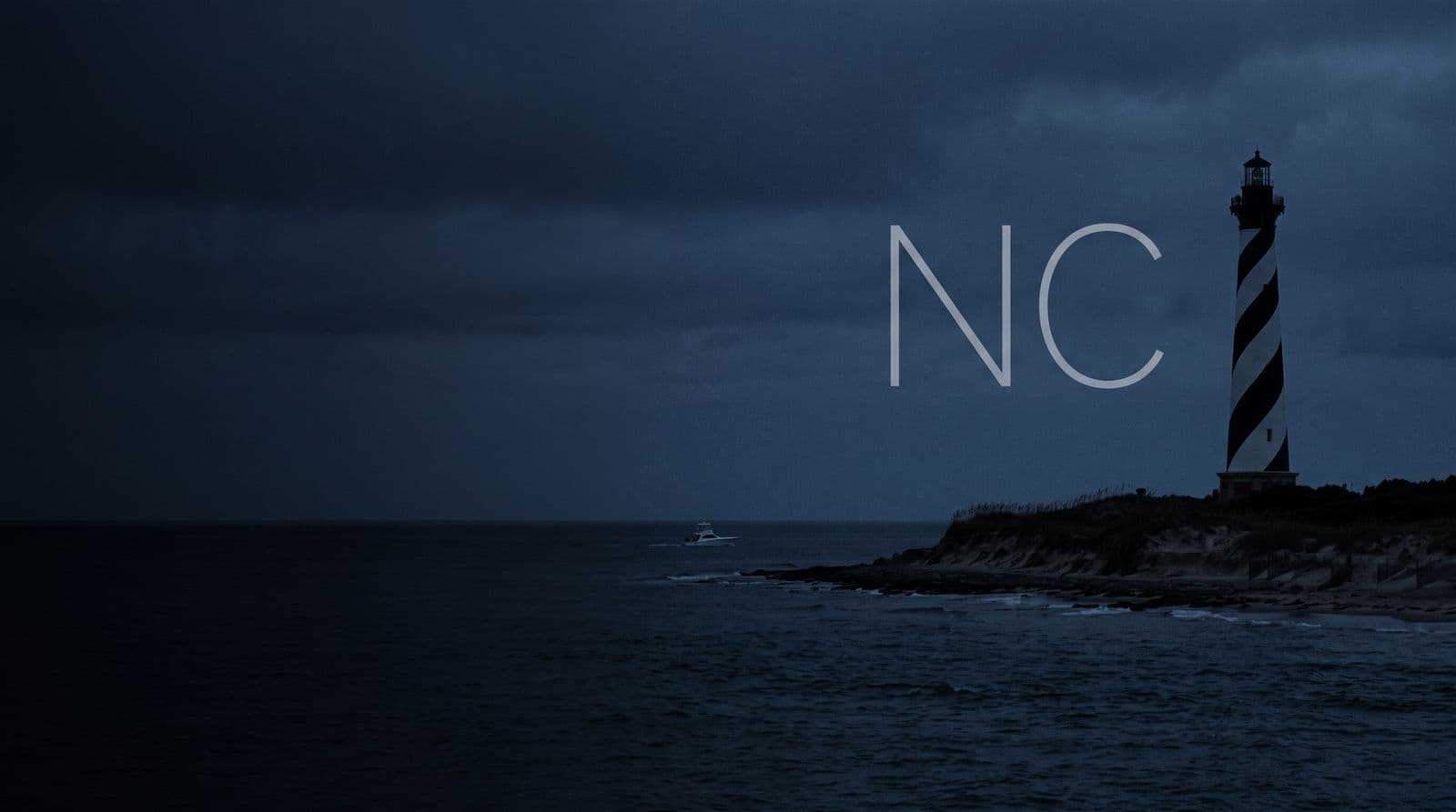 The Cape Hatteras lighthouse on the Outer Banks at dusk, a boat offshore, with the letters NC in the sky