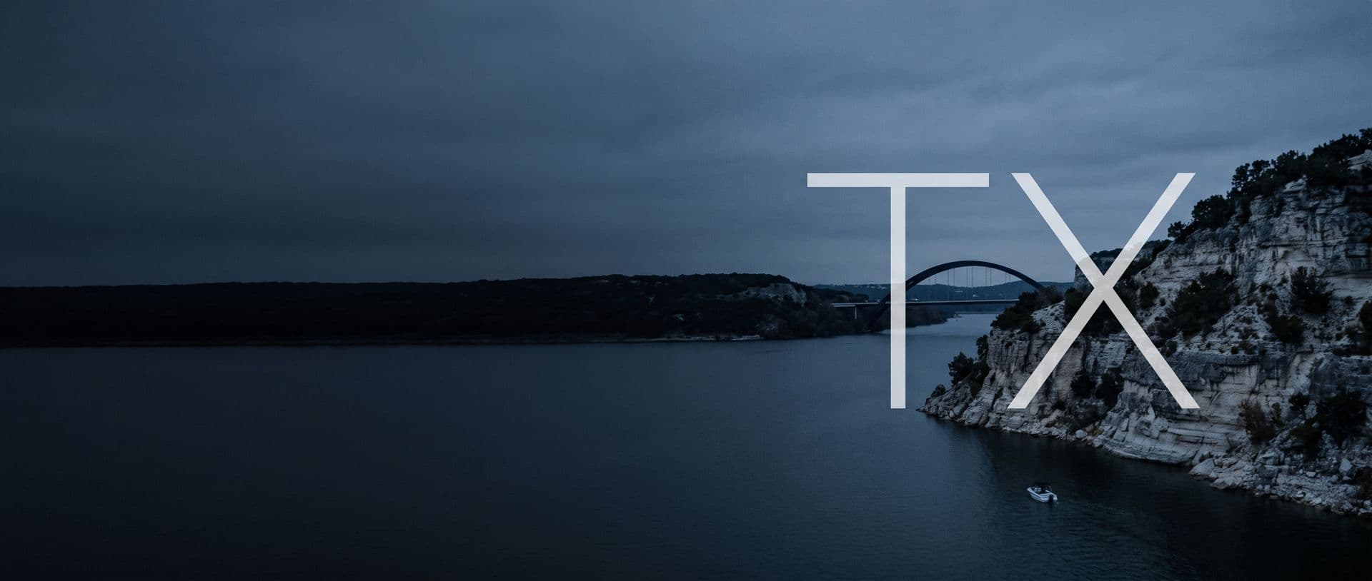 Limestone cliffs and the 360 bridge over Lake Travis at dusk, a boat on the water below, with the letters TX in the sky