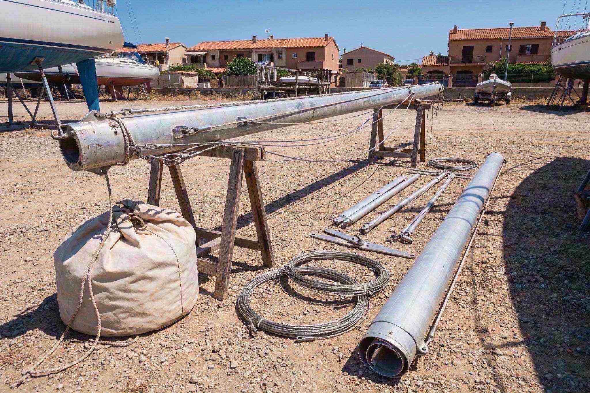 A sailboat mast lying on trestles in a boatyard with its shrouds, spreaders and furling foil laid out beside it