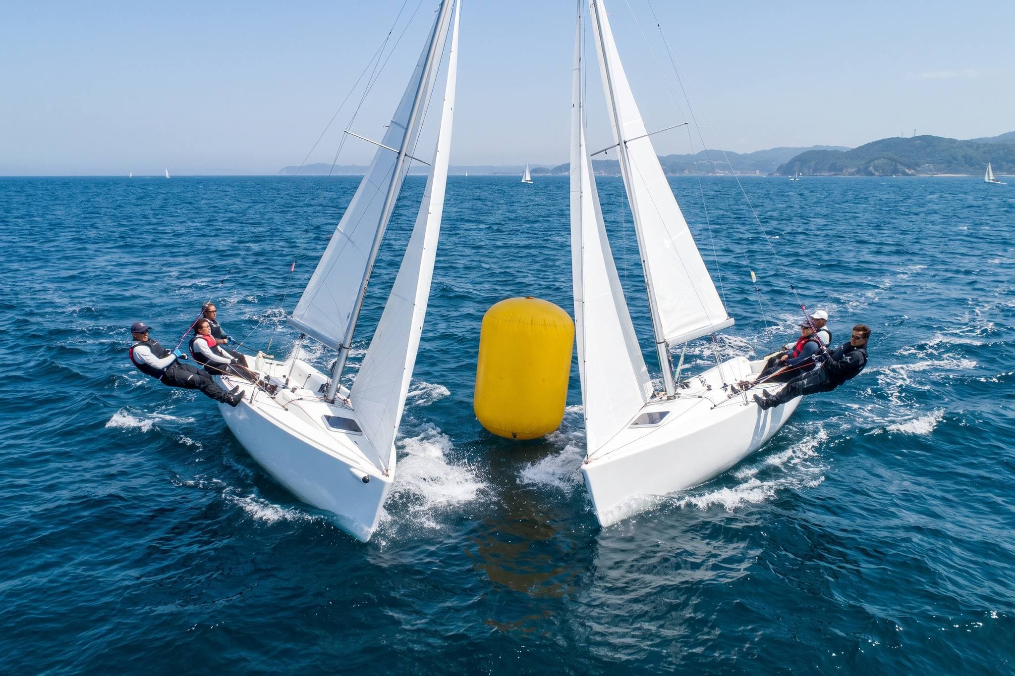 Two white keelboats rounding a yellow racing mark close together in bright sun