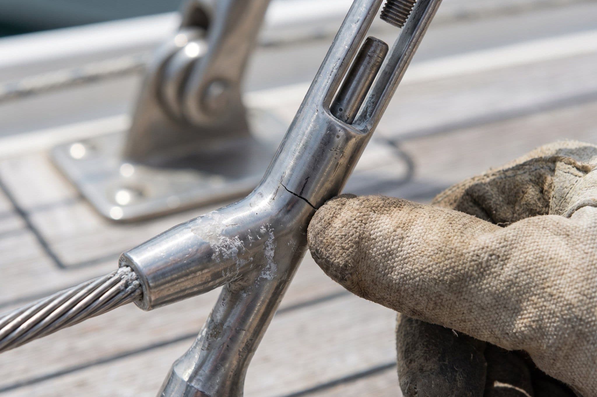 Close-up of a hairline crack at the swage terminal of a sailboat shroud, a gloved finger pointing at it