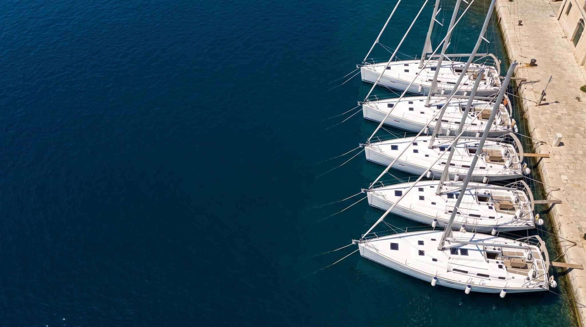 Aerial view of yachts med mooring stern-to a stone marina quay in clear blue water