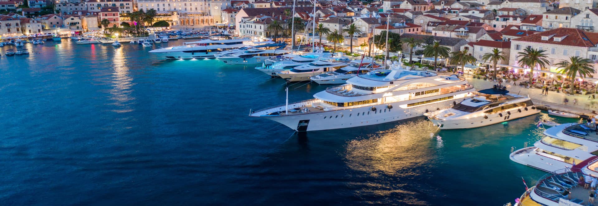 Motor yachts moored stern-to along a Mediterranean harbour waterfront at blue hour, open water in the foreground