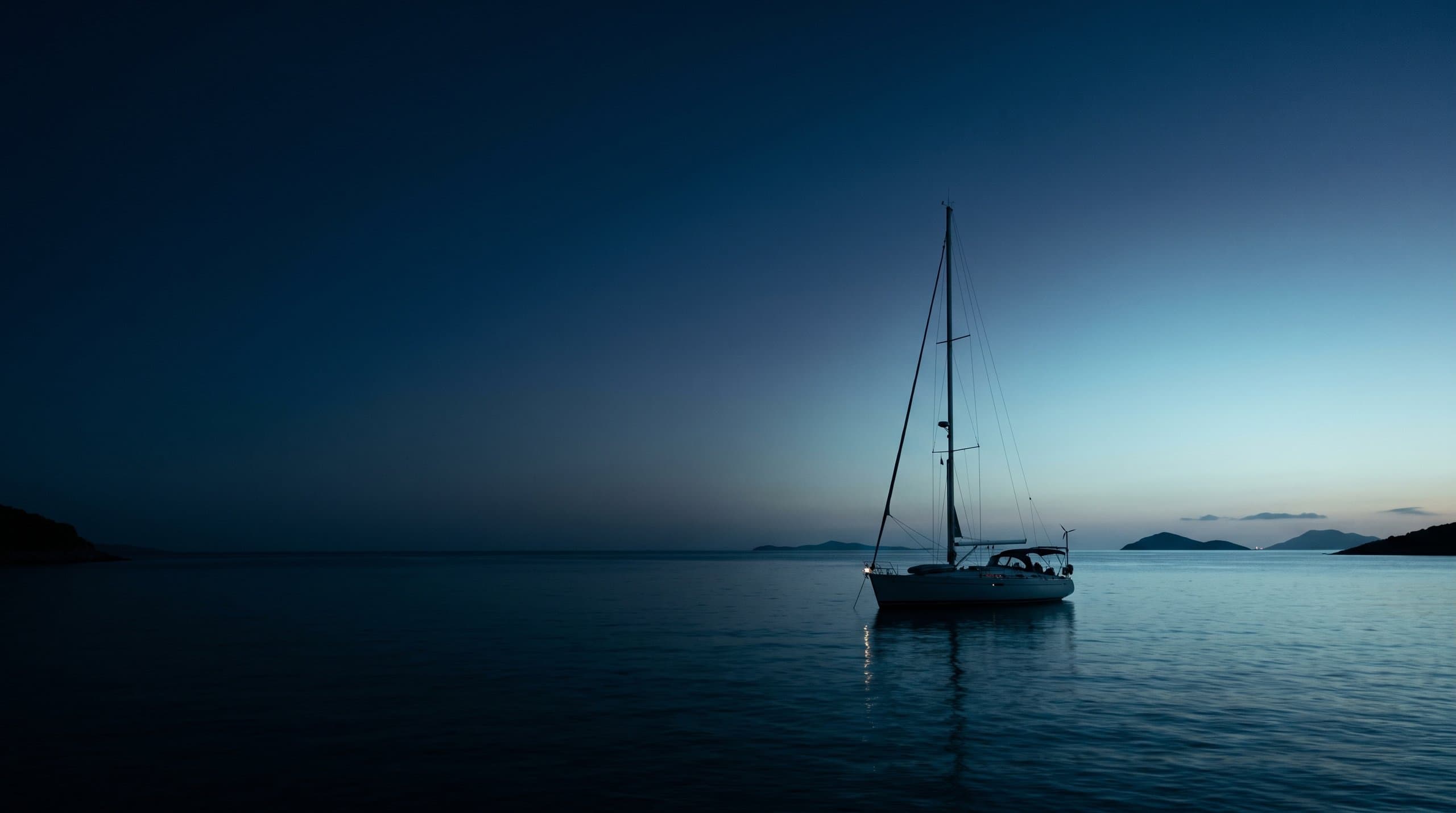 A 40-foot cruising sailing yacht moored at a marina dock at dusk, warm cabin lights glowing through the portholes, potted plants and a bicycle on the dock, representing a liveaboard life afloat.