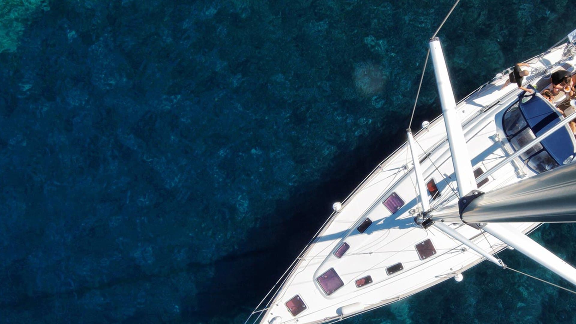 Luftaufnahme von oben auf eine Einrumpf-Segelyacht über tiefblauem Wasser, Mast und Vordeck senkrecht von oben