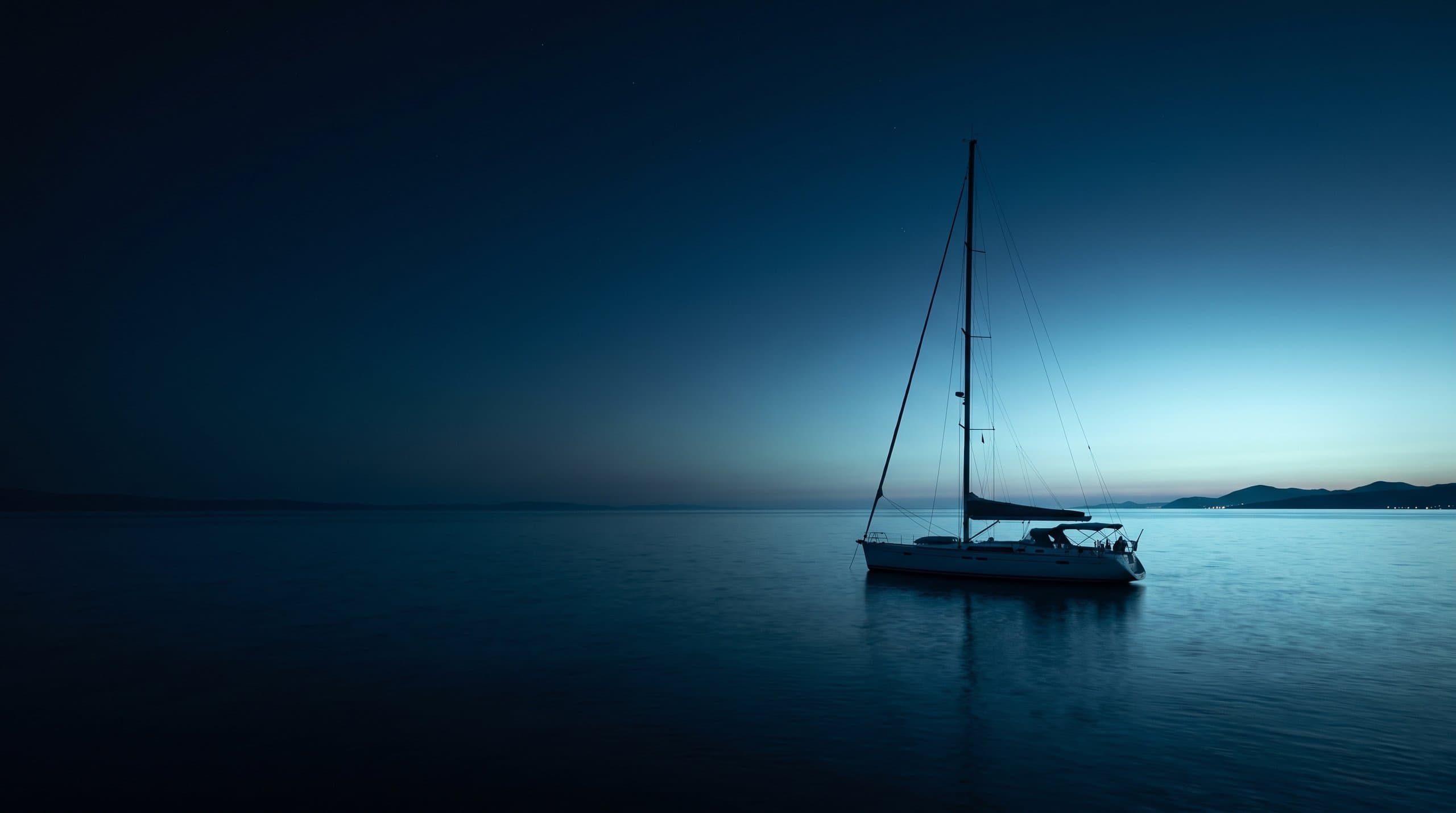 Barca a vela all'ancora in una baia riparata della costa dalmata in Croazia, con collina di calcare coperta di pini e un borgo di pietra sullo sfondo nella luce dorata